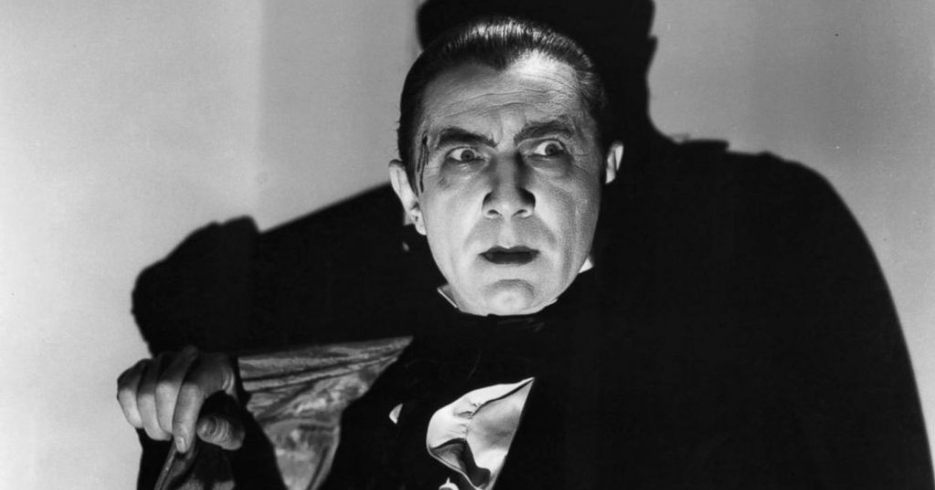 Dracula with a shocked expression wearing a formal suit and cape with a dramatic shadow behind him.
